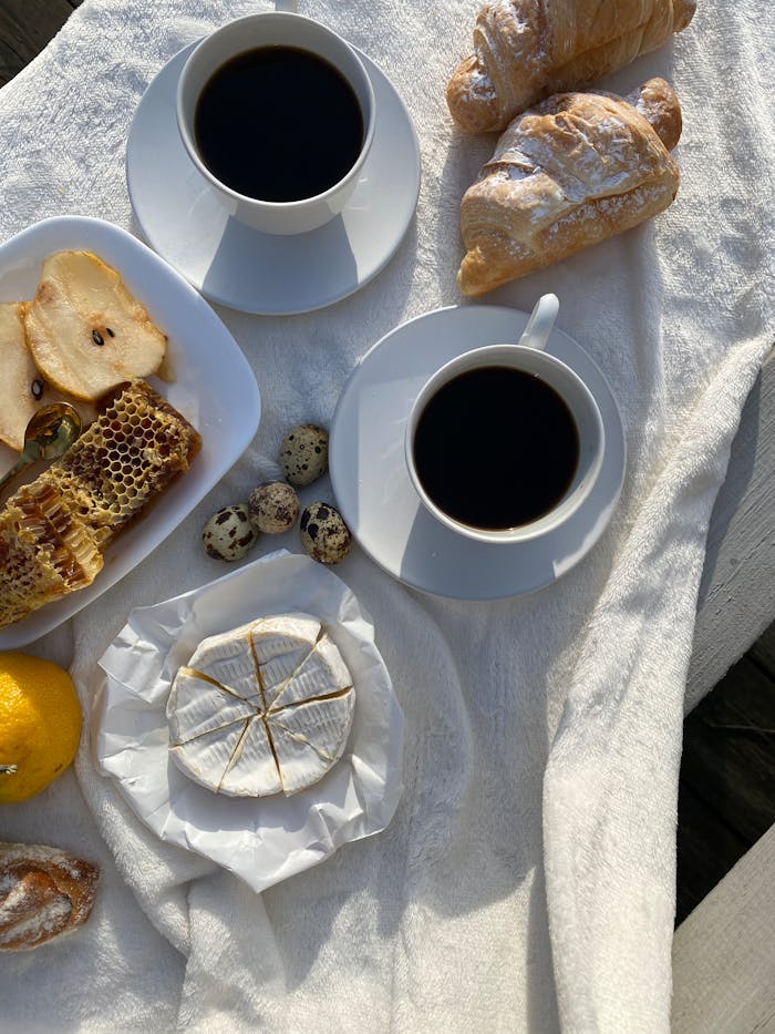 Charming breakfast scene with coffee, croissants, honeycomb, cheese, and quail eggs.